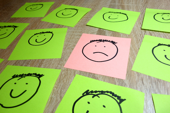 Single sad face drawing among happy smiling ones