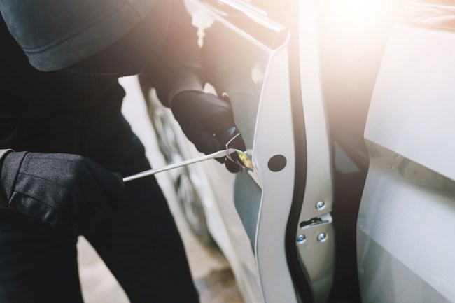 Close up hand pulling the handle of a car thief wearing black clothes and glove stealing automobile trying door handle to see if vehicle is unlocked trying to break into. car theft concept.