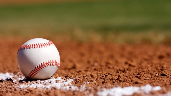 A baseball rests along the foul line on the infield clay.