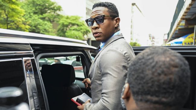 jonathan majors in a suit getting into a car