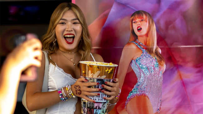 movie goer takes picture in front of Taylor Swift Eras movie poster