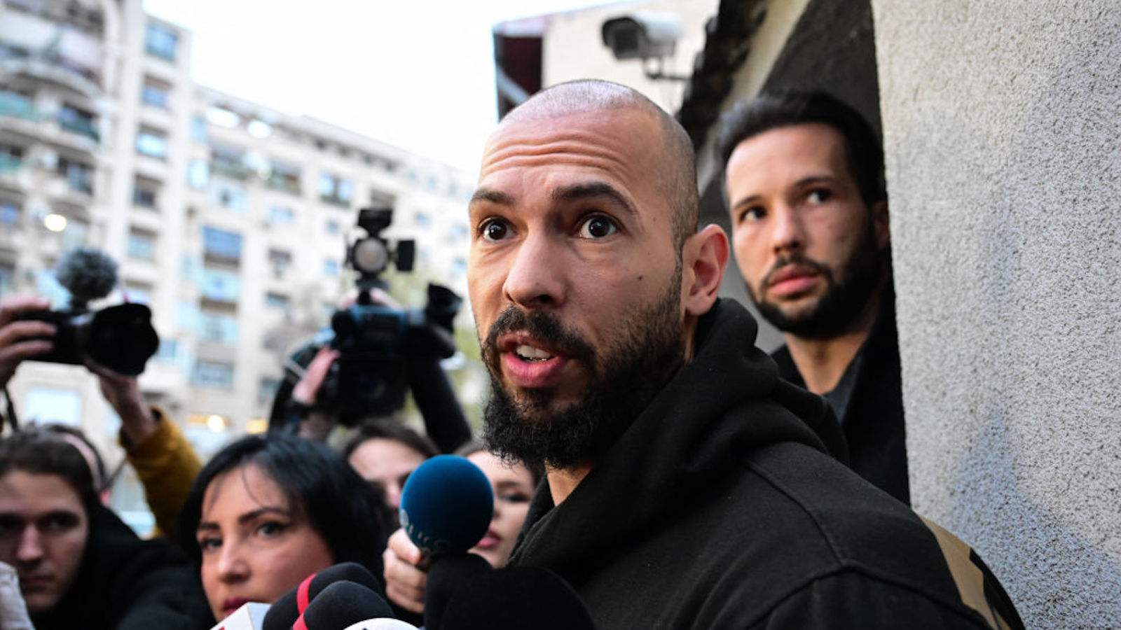 British-US former professional kickboxer and controversial influencer Andrew Tate (front) and his brother Tristan Tate (back R) speak to journalists after having been released from detention in Bucharest, Romania on March 12, 2024, after they appeared in a Bucharest court after Romanian police detained them over UK sex offence charges. A Bucharest court on March 12 granted a request to extradite controversial influencer Andrew Tate to the UK over sex offence charges, but only after the conclusion of legal proceedings in Romania in a separate case. The Bucharest appeals court ruling "orders the execution of the warrant of arrest issued on 19 January 2024" by the Westminster Magistrates' Court, but postpones extradition "until the final resolution of the case" in Romania, which could take years. (Photo by Daniel MIHAILESCU / AFP)